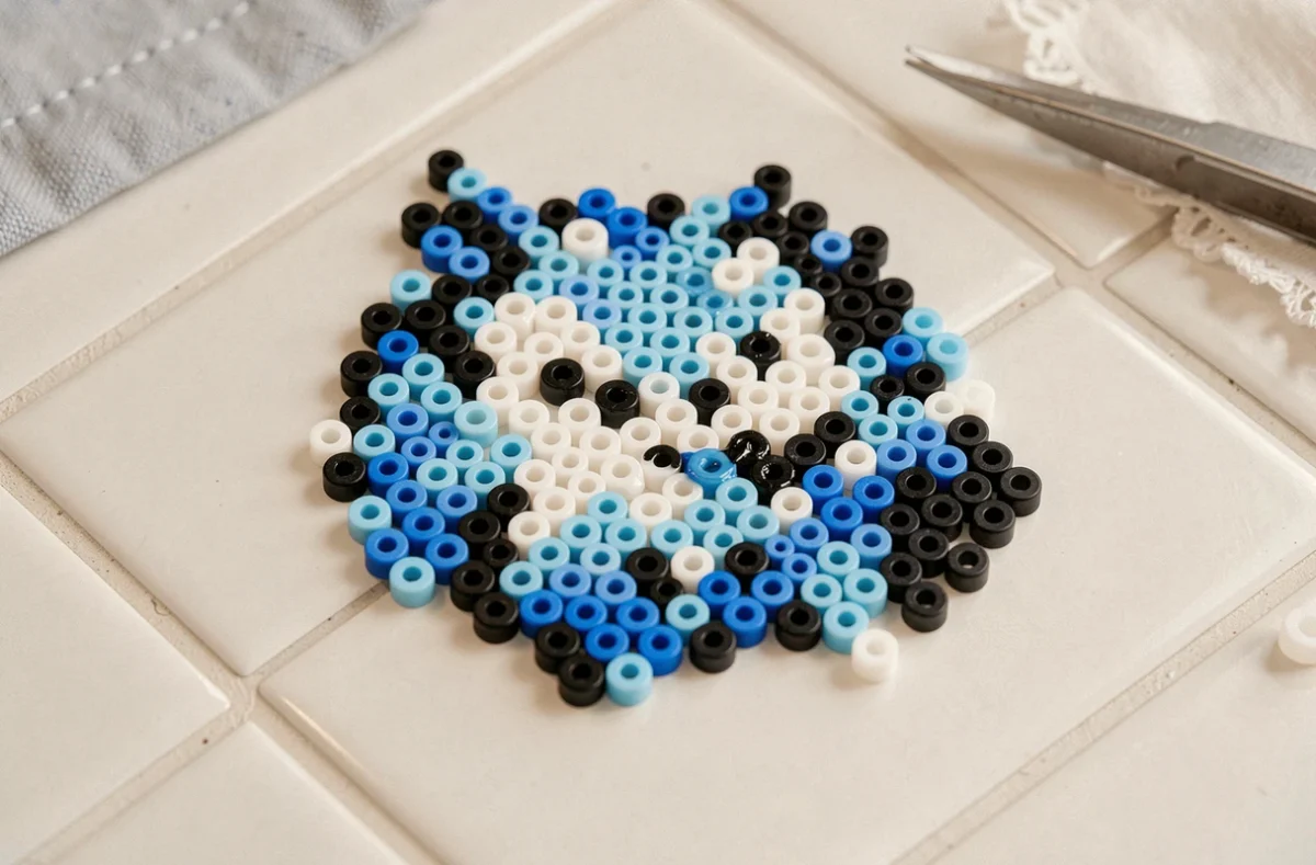 Gros plan sur un modèle perles à repasser représentant Stitch en bleu et noir, posé sur un carrelage blanc avec des accessoires de création